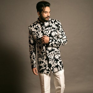 K&ouml;nnte beinhalten: Ein Mann tr&auml;gt einen schwarzen Blazer mit wei&szlig;em Muster, wei&szlig;e Hose und schwarze Schuhe.