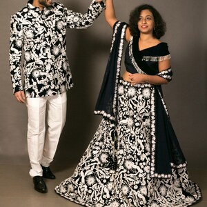 K&ouml;nnte beinhalten: Ein Paar in traditioneller indischer Kleidung. Die Frau tr&auml;gt einen schwarzen und wei&szlig;en bestickten Lehenga mit einem blauen Dupatta. Der Mann tr&auml;gt eine schwarze und wei&szlig;e gemusterte Jacke mit einer wei&szlig;en Hose.