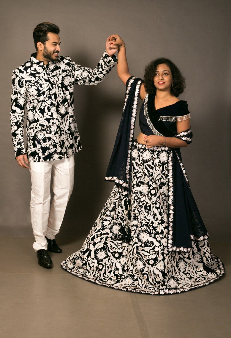 K&ouml;nnte beinhalten: Ein Paar in traditioneller indischer Kleidung. Die Frau tr&auml;gt einen schwarzen und wei&szlig;en bestickten Lehenga mit einem blauen Dupatta. Der Mann tr&auml;gt eine schwarze und wei&szlig;e gemusterte Jacke mit einer wei&szlig;en Hose.