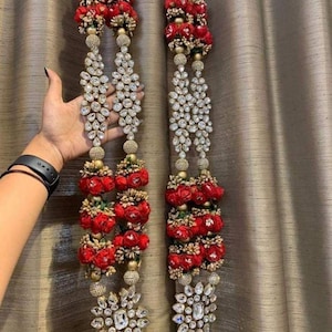 Può includere: Due lunghe ghirlande decorative con fiori di stoffa rossi e perline di cristallo. Le ghirlande sono appese a uno spago dorato e hanno un grande ciondolo di cristallo in fondo.