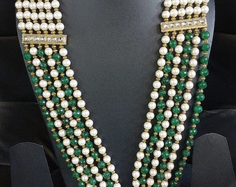 Op de afbeelding: Een meerstrengige ketting met witte en groene kralen. De ketting heeft een gouden hanger met een bloemmotief en een kwast.