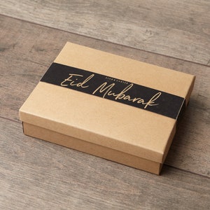 May include: A brown cardboard gift box with a black ribbon and the text "Eid Mubarak" in gold lettering.