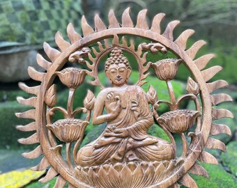 May include: A wooden carving of Buddha seated in lotus position, surrounded by a sunburst design. The sculpture is a warm brown color, with intricate details in the carving. The Buddha is seated on a lotus flower, with other lotus flowers around him.