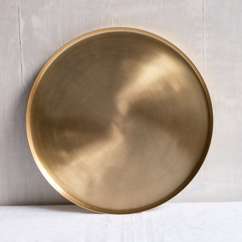 May include: A round, brushed gold metal serving tray. The tray has a smooth, polished surface.