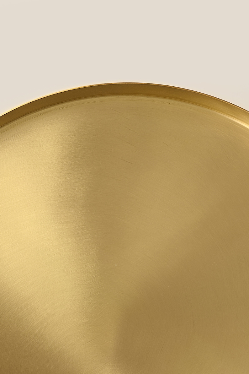 May include: A gold-colored metal tray with a smooth, brushed finish. The tray is round and has a slightly raised edge.