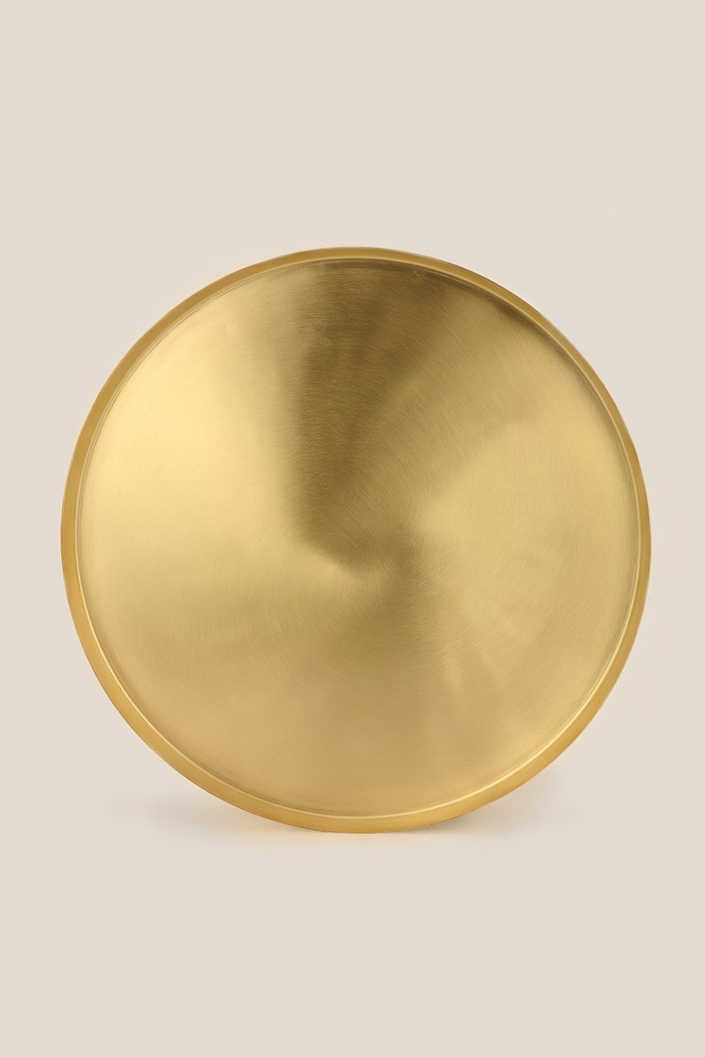 May include: A round, gold-colored metal tray with a smooth, brushed finish.