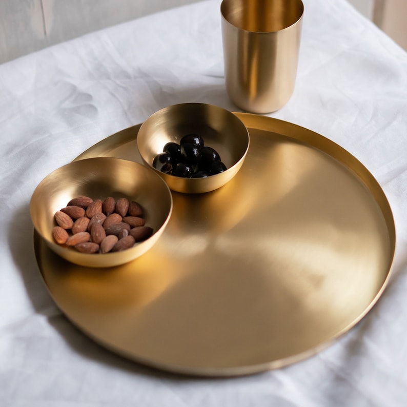 May include: A gold-toned serving tray with two smaller bowls. One bowl contains almonds, and the other bowl contains black olives.