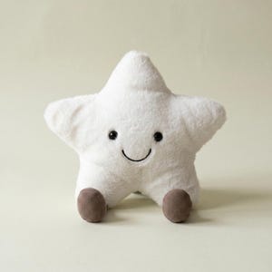 May include: A plush star-shaped toy with soft white fur, featuring two small black embroidered eyes and a simple curved black mouth. The star has two small, round, brown corduroy feet attached at the bottom, giving it a seated appearance.