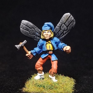 May include: A miniature figurine of a winged fairy with blue wings, a blue hat, and a red and orange outfit. The fairy is holding a small axe in its right hand and is standing on a green base.