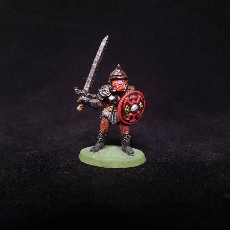 Pu&ograve; includere: Una figurina in miniatura dipinta di un guerriero che indossa un'armatura nera e un elmo rosso con uno scudo rosso e dorato. Il guerriero tiene una spada d'argento.