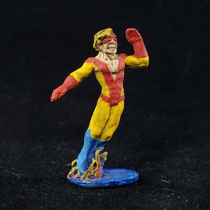 May include: A painted miniature figurine of a superhero wearing a yellow and red costume with a blue and yellow surfboard. The superhero has a yellow mask with a red stripe across the eyes.