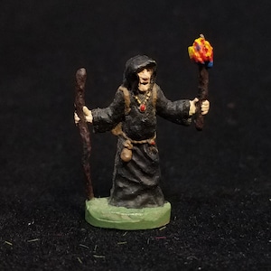 May include: A painted miniature figure of a wizard wearing a black hooded robe, holding a staff and a torch. The wizard has a red gem necklace and a pouch on their belt.