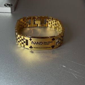 Puede incluir: Una pulsera dorada con una placa rectangular grabada con el texto "NWD New Wave Design POKER RUN CHAMPION". La pulsera presenta un dise&ntilde;o de eslabones de cadena y s&iacute;mbolos de naipes.