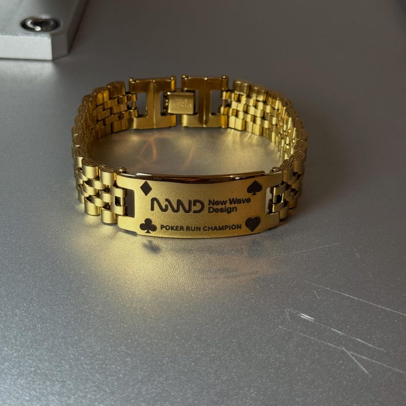 Puede incluir: Una pulsera dorada con una placa rectangular grabada con el texto "NWD New Wave Design POKER RUN CHAMPION". La pulsera presenta un dise&ntilde;o de eslabones de cadena y s&iacute;mbolos de naipes.