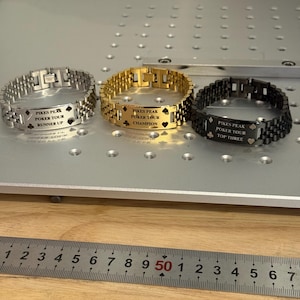 Puede incluir: Tres pulseras met&aacute;licas en plata, oro y negro, cada una grabada con "PIKES PEAK POKER TOUR" y una clasificaci&oacute;n: Runner Up, Champion y Top Three. Las pulseras se exhiben sobre una superficie gris claro con un fondo de madera.