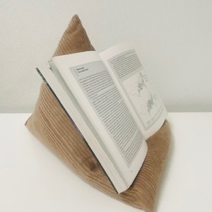 Könnte beinhalten: Ein brauner Cord-Buchständer mit einem darauf liegenden Buch. Das Buch ist geöffnet und hat Text auf den Seiten.