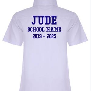 May include: A white short-sleeved shirt with a button-down collar. The back of the shirt displays the name "JUDE", the text "SCHOOL NAME", and the years "2019 - 2025" in blue block letters. The shirt is made of a smooth fabric, possibly cotton.