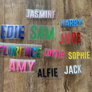 May include: A collection of personalised name labels in various colours, including blue, green, red, yellow, pink, and white. The names include Edie, Sam, Jasmine, Harry, Jude, Florence, Lottie, Sophie, Amy, Alfie, and Jack.