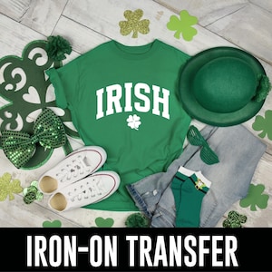May include: Green t-shirt with the word "IRISH" in white letters and a shamrock design. The shirt is on a white wood background with green shamrock decorations.
