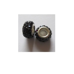 Könnte beinhalten: Zwei schwarze Kristallperlen-Abstandshalter für die Schmuckherstellung. Die Perlen sind rund und haben einen silbernen Metallkern. Die Perlen sind mit kleinen schwarzen Kristallen bedeckt.