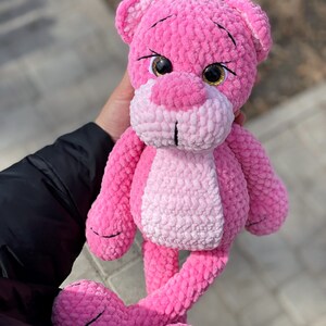 May include: Pink crocheted plush toy shaped like a bear with large, sparkly eyes. The bear has long, thin legs and a pink and white ombre color scheme.