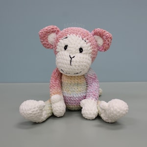 May include: A crocheted monkey plush toy featuring a soft, textured yarn in variegated pastel shades of pink, yellow, blue, and white. The monkey has a white face, black embroidered eyes, a nose, and a mouth, with the word Matilanz visible above.