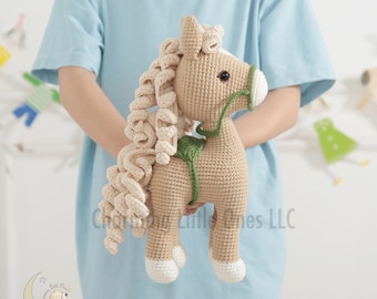May include: A tan crochet horse toy featuring a long, curly cream-colored mane, a white muzzle, white hooves, and a green bridle and saddle. The text Charming Little Ones LLC is visible in the center, with a small logo in the bottom left corner.