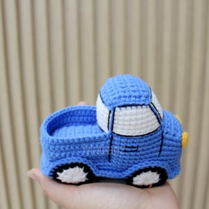Handmade crocheted toy car in vibrant blue with white accents, featuring a classic design with black wheels and yellow details.
