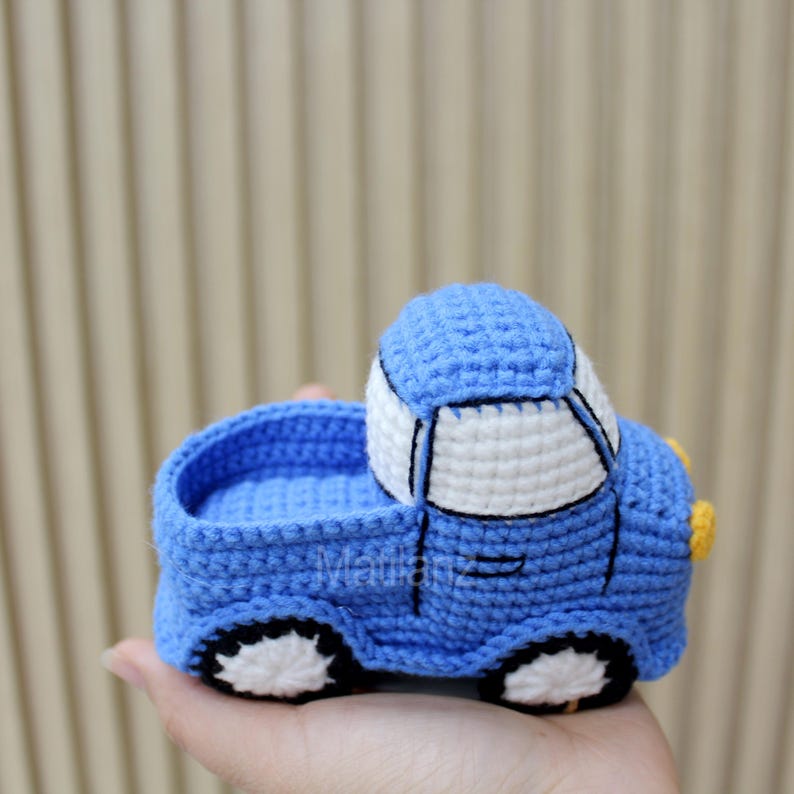 Handmade crocheted toy car in vibrant blue with white accents, featuring a classic design with black wheels and yellow details.