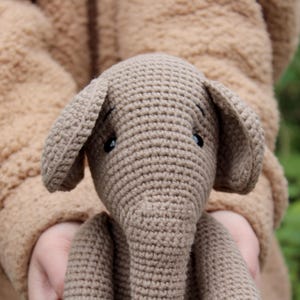 Handmade crochet elephant toy in soft beige wool with textured pattern, large expressive eyes, and dangling ears.