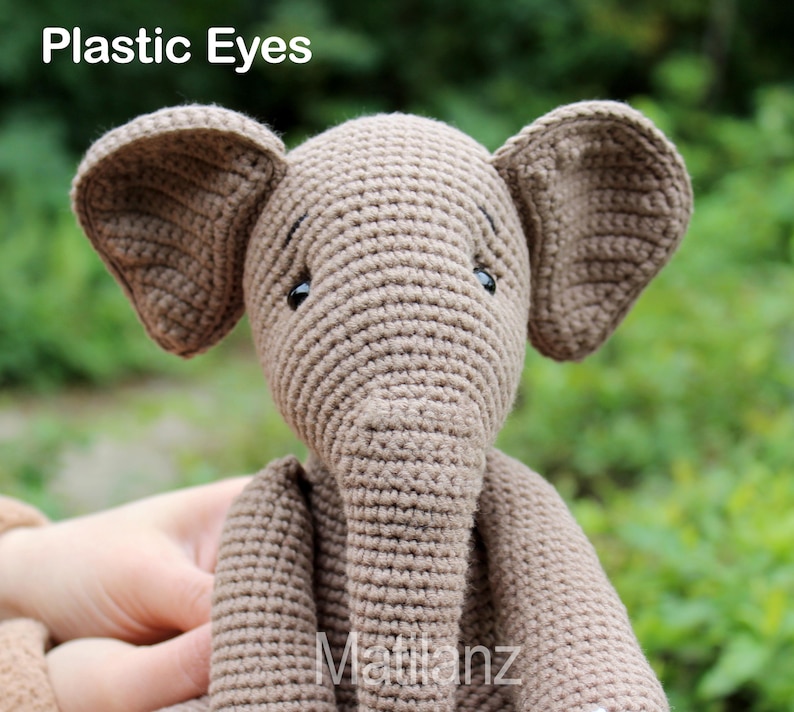 Handmade elephant-shaped toy crafted from beige crocheted cotton yarn, featuring floppy ears and plastic eyes.
