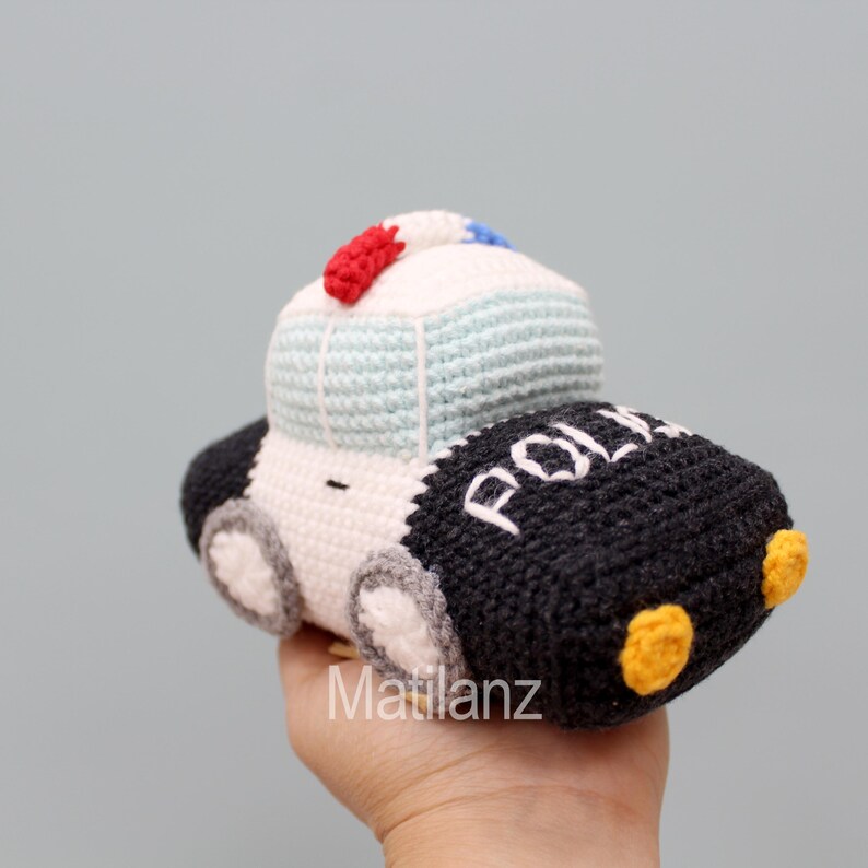 Handmade crocheted police car toy in black, white, blue, red, and yellow, featuring a classic car shape with wheels, lights, and "POLICE" lettering on the side.