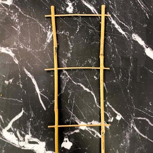 May include: A wooden trellis made of natural bamboo sticks. The trellis is made of four horizontal pieces of bamboo and two vertical pieces of bamboo. The trellis is on a black and white marble background.