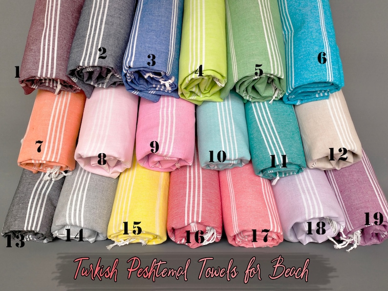 May include: A collection of 19 Turkish Peshtemal towels in various colors, rolled up and arranged in rows. The towels are made of cotton and have a striped pattern. The text "Turkish Peshtemal Towels for Beach" is printed at the bottom of the image.