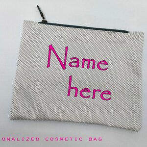 May include: White zippered cosmetic bag with a black zipper and a pink embroidered design that says "Name here".