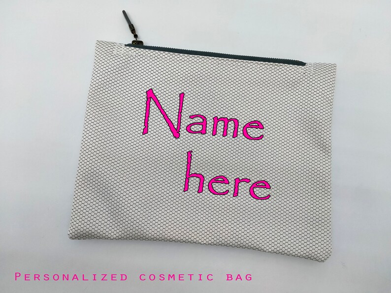May include: White zippered cosmetic bag with a black zipper and a pink embroidered design that says "Name here".
