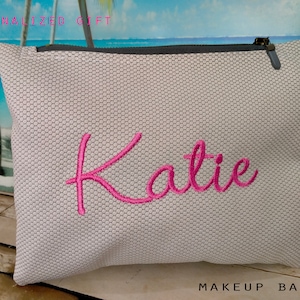 May include: A white mesh makeup bag with a grey zipper and the name "Katie" embroidered in pink.