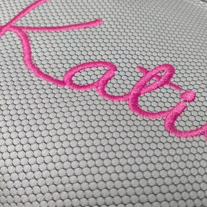 May include: Pink embroidered name "Katie" on a white mesh fabric.