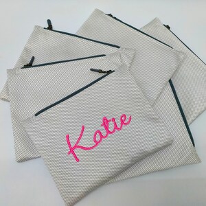 May include: Set of five white mesh zippered pouches with a dark blue zipper and a pink embroidered name "Katie" on one pouch.