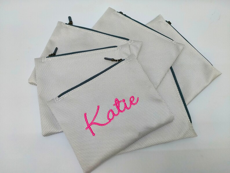 May include: Set of five white mesh zippered pouches with a dark blue zipper and a pink embroidered name "Katie" on one pouch.