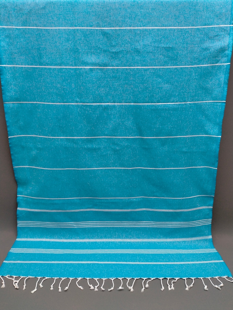 May include: A turquoise and white striped beach towel with white fringe. The towel is made of cotton and is soft and absorbent.