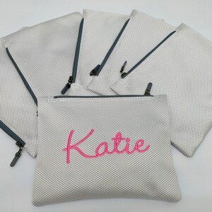 May include: Set of six white mesh zippered pouches with grey trim. One pouch has the name "Katie" embroidered in pink.