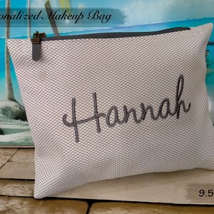 May include: White mesh makeup bag with a grey zipper and a grey embroidered name "Hannah". The bag measures 9.5 x 7.5 inches.