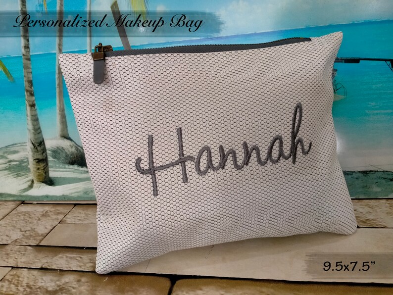 May include: White mesh makeup bag with a grey zipper and a grey embroidered name "Hannah". The bag measures 9.5 x 7.5 inches.