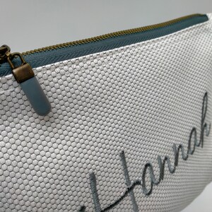 May include: White zippered pouch with a grey mesh fabric and the name "Hannah" embroidered in grey thread.