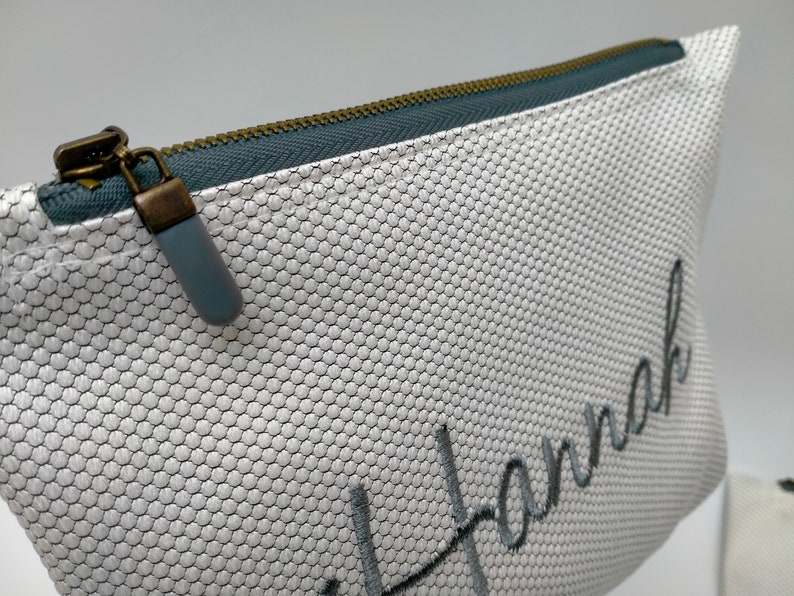 May include: White zippered pouch with a grey mesh fabric and the name "Hannah" embroidered in grey thread.