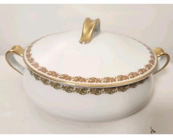 May include: White porcelain serving bowl with lid. The bowl features gold handles and a gold handle on the lid. A decorative band of gold, green, and red floral design encircles the rim of the bowl and lid. A classic piece for serving.