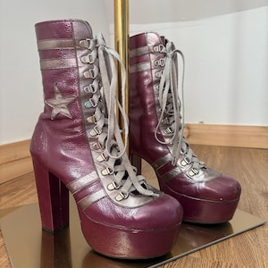 May include: A pair of high-heeled platform boots with a silver and burgundy color scheme. The boots have a lace-up front and a star detail on the side.