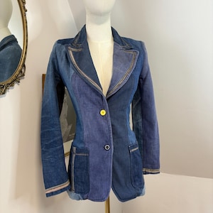 Peut inclure: Un blazer en jean bleu patchwork, présenté sur un mannequin. Le blazer a un revers cranté, deux poches avant et une fermeture à un seul bouton. Les manches ont une bordure contrastée et le vêtement est taillé pour une silhouette ajustée.