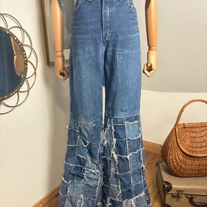 May include: High-waisted blue denim jeans featuring a solid upper section and wide, flared legs constructed from a patchwork of various blue denim fabric squares with frayed, raw edges throughout the lower portion of the garment.